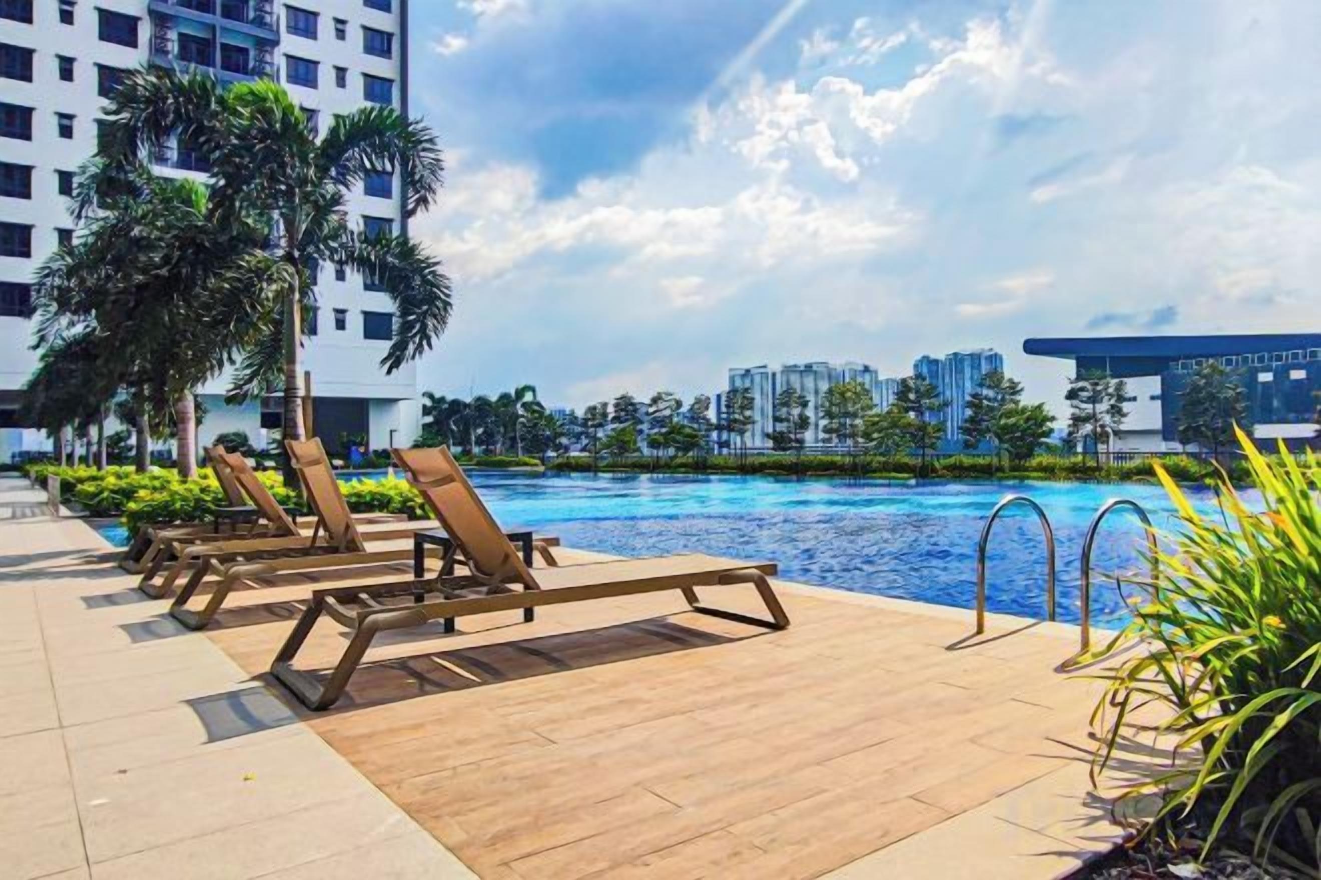 A poolside area with lounge chairs, a swimming pool, and a view of a cityscape with buildings in the background.