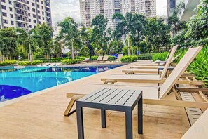 A poolside area with lounge chairs and a table, surrounded by greenery and high-rise buildings in the background. - Sunset Lake View at M-Luna Kepong by HCK (Kuala Lumpur)