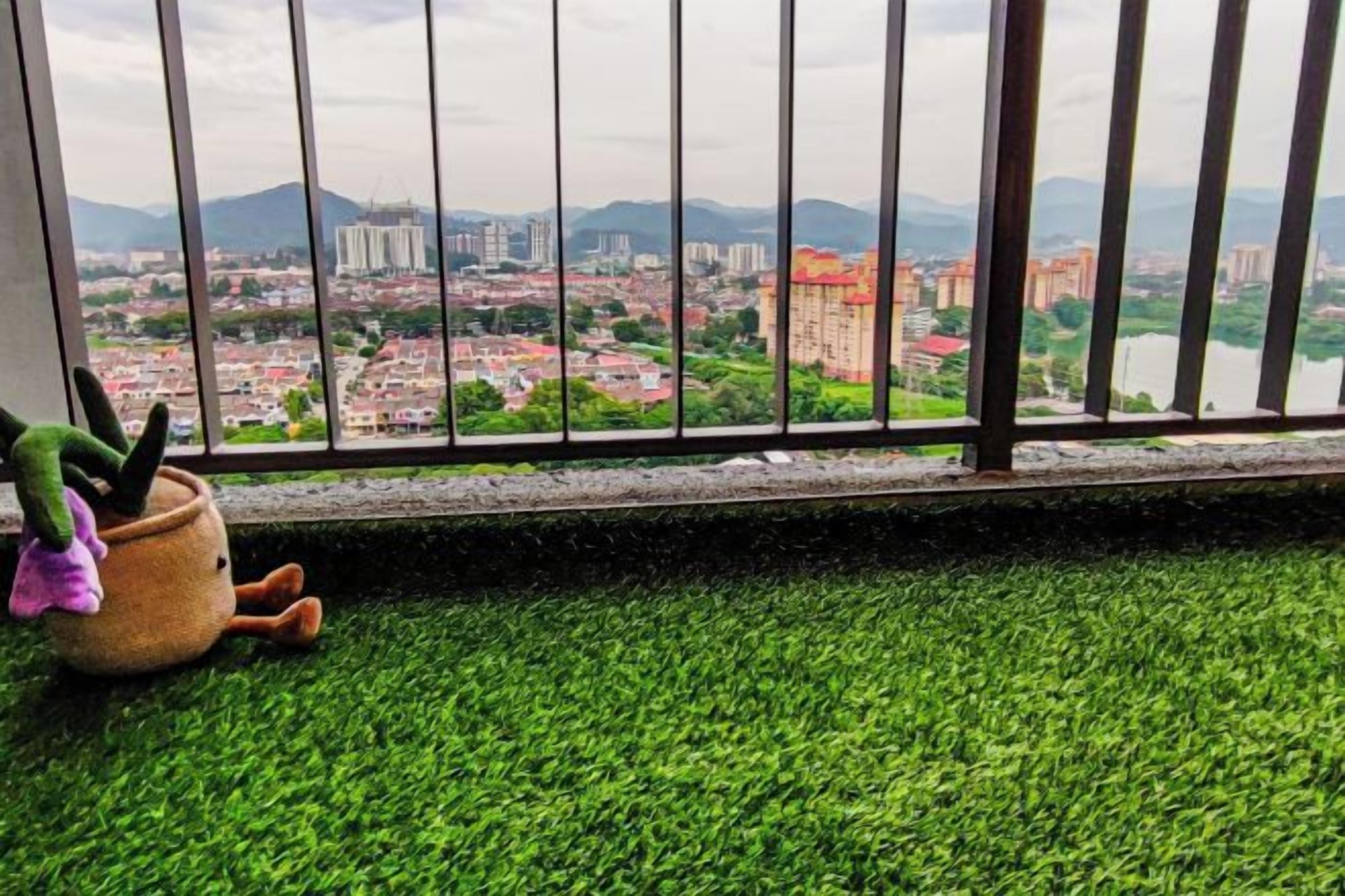 Vista a través de una ventana con barandilla, suelo de césped artificial verde y una maceta con un cactus.