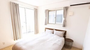 A bedroom with a bed, a bedside table, a window with curtains, and a wall-mounted air conditioning unit. - MoonLight inn Free parking (Dazaifu)