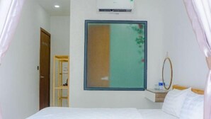 A bedroom with a bed, a wooden wardrobe, a mirror, and a window with a view of greenery. - HUYNH's HOUSE 4 Bedroom Apartment (Phu Quoc Island)