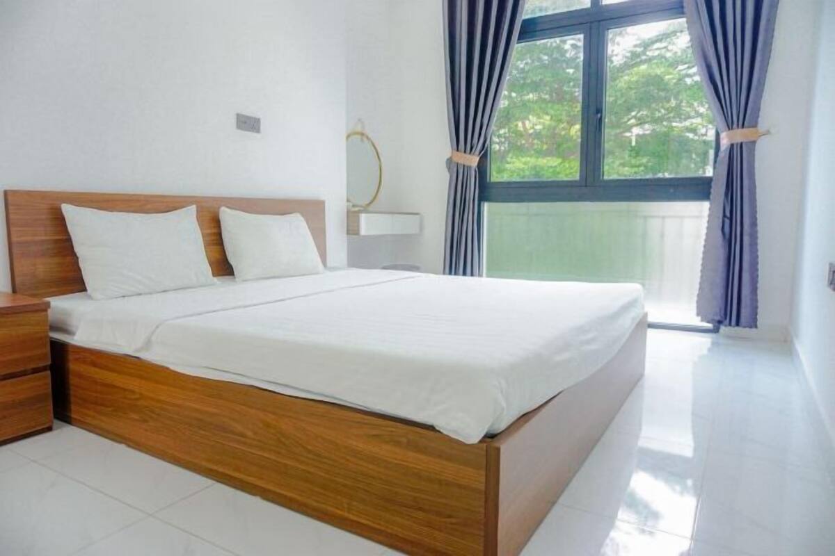 A neatly made bed with a wooden headboard, a bedside table, and a window with curtains.