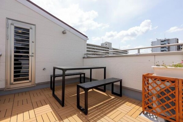 A rooftop terrace with a table and bench, a door with a window, and a railing. - QingChen zhi Shu (Osaka)