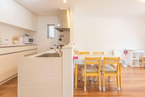 A modern kitchen with white cabinets, a microwave, and a dining area with wooden chairs. - QingChen zhi Shu (Osaka)