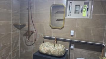 A bathroom with a marble wall, a sink with a marble basin, a handheld showerhead, and a mirror.