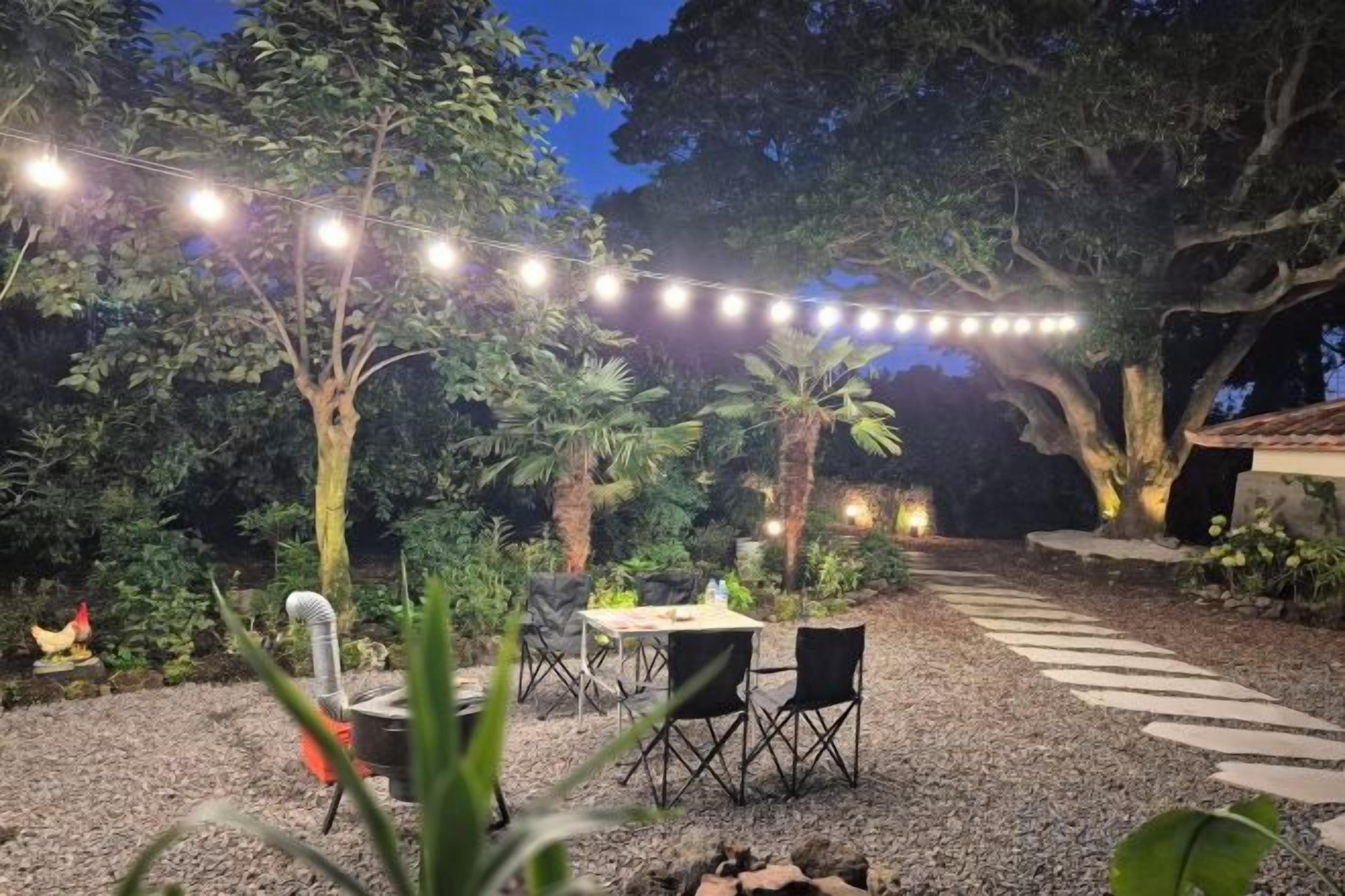 An outdoor dining area with string lights, a table, chairs, and a gravel path.