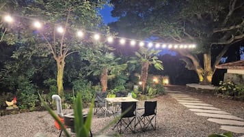 An outdoor dining area with string lights, a table, chairs, and a gravel path.