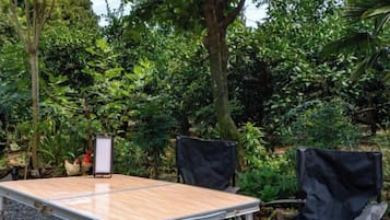 An outdoor table with a screen, two covered chairs, and a natural backdrop of trees and foliage.