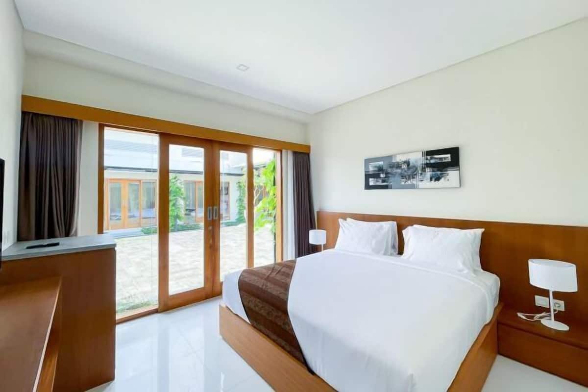 A hotel room with a large bed, a desk, a chair, a TV, and a sliding glass door leading to an outdoor area.