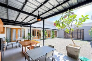 A covered patio area with a dining table and chairs, a potted plant, and a view of the surrounding area. - Aldan Guest House Syariah (Bali)