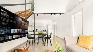 Un salon moderne doté d’un téléviseur à écran plat, d’un canapé, d’une table basse et d’un coin repas avec des chaises et une table.