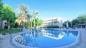 Une piscine à bord incurvé, entourée de palmiers et avec un bâtiment en arrière-plan.
