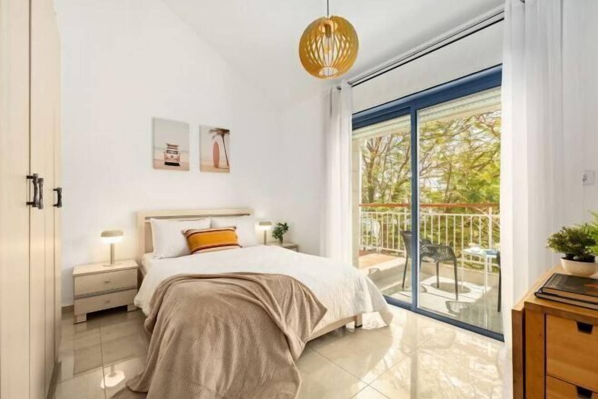 Un dormitorio moderno con una cama grande, una mesita de noche, una lámpara de noche y vistas a un balcón con mobiliario exterior.