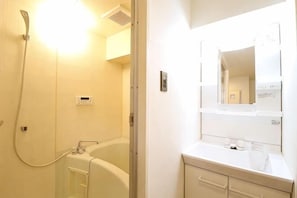 A bathroom with a bathtub, a shower, a mirror, and a sink. - Amistá.You (Osaka)