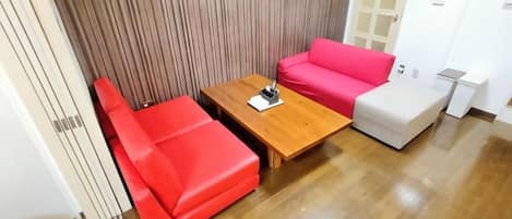 A room with a wooden coffee table, a red sofa, and a white ottoman.