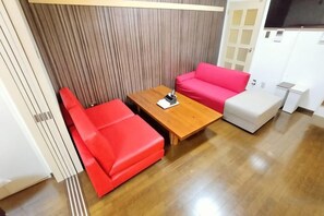 A room with a wooden coffee table, a red sofa, and a white ottoman. - Amistá.You (Osaka)