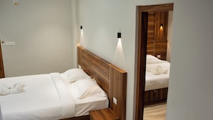 A hotel room with a wooden headboard, a bedside table, and a mirror reflecting the bed. - Kanak Residency Thalassary (Thalassery)