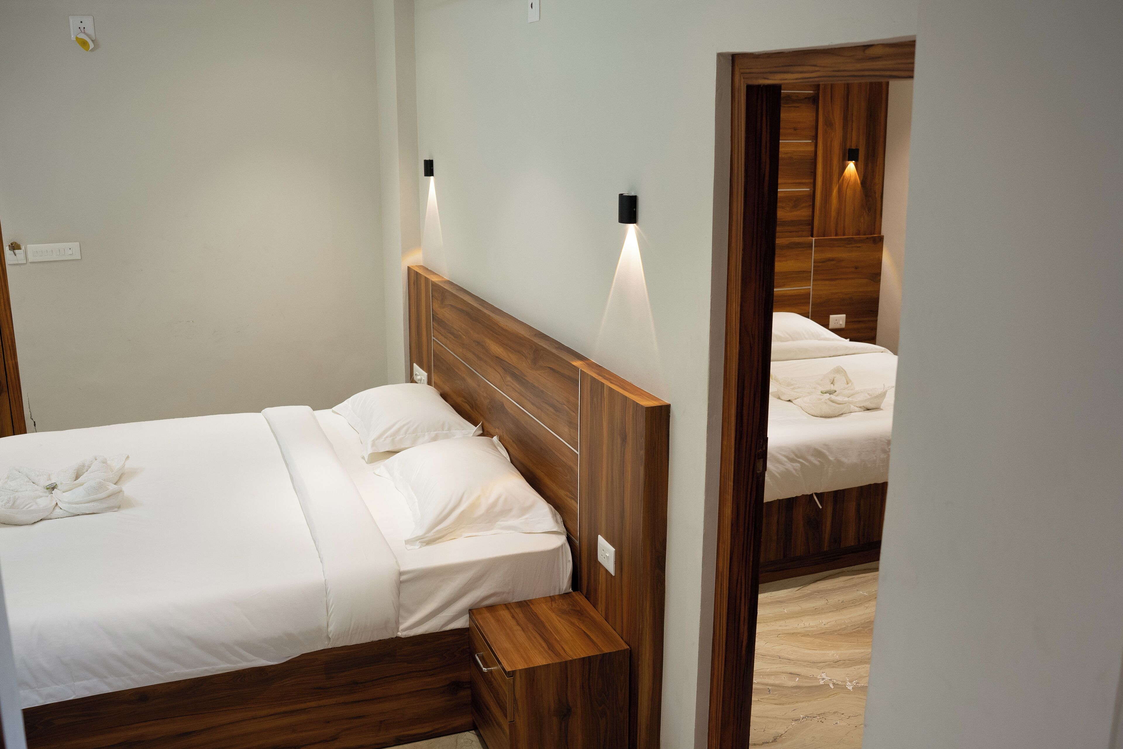 Una habitación de hotel con cabecera de madera, una mesita de noche y un espejo que refleja la cama.