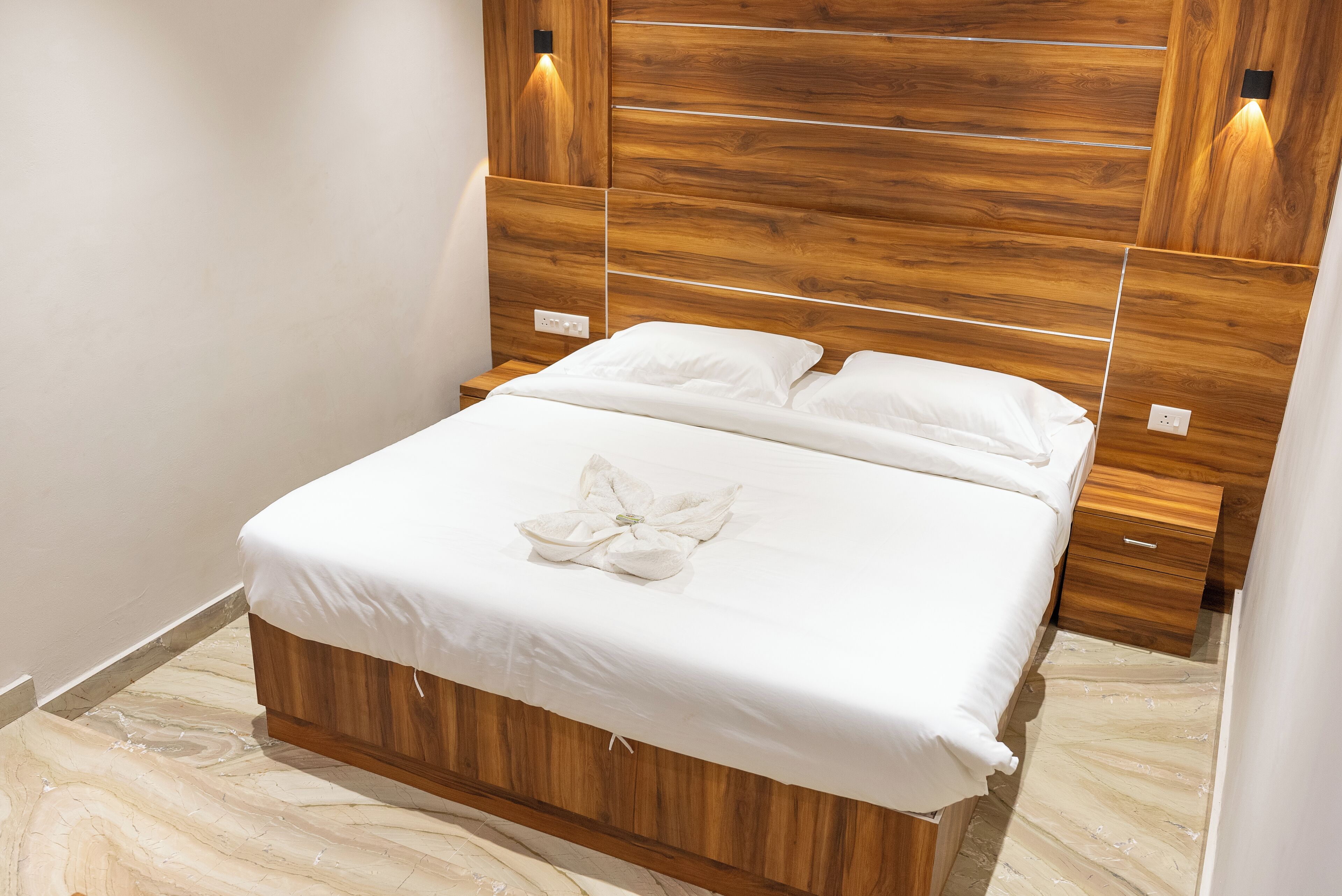 A neatly made bed with white linens and a decorative flower arrangement, set against a wooden headboard with integrated lighting.