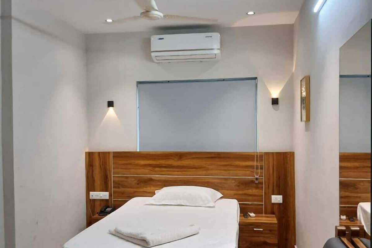 Een moderne hotelkamer met een houten hoofdbord, een enkel bed, een nachtkastje, een stoel, een grote spiegel en een airconditioning.
