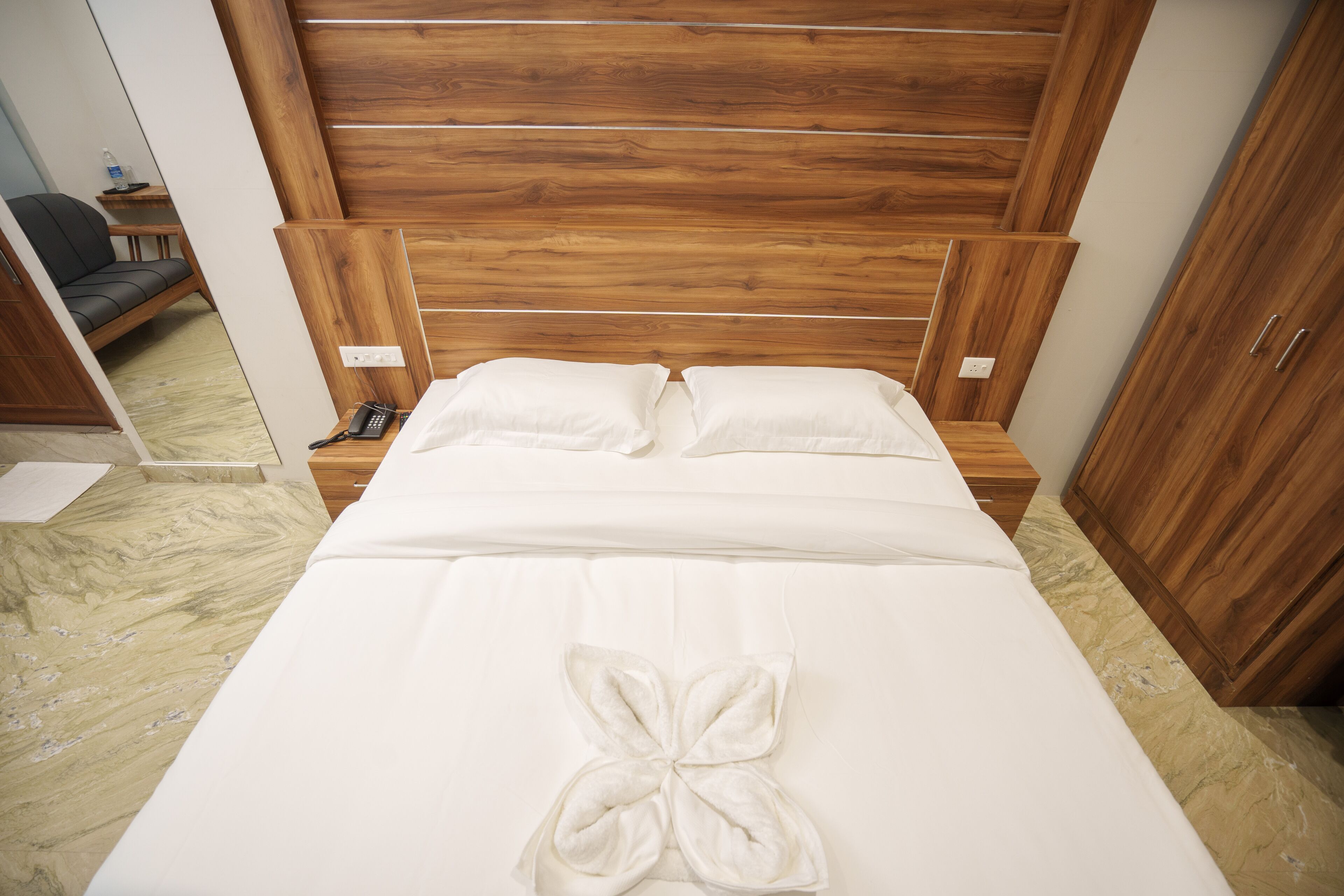A neatly made bed with a wooden headboard, a bedside table with a lamp, and a wardrobe.