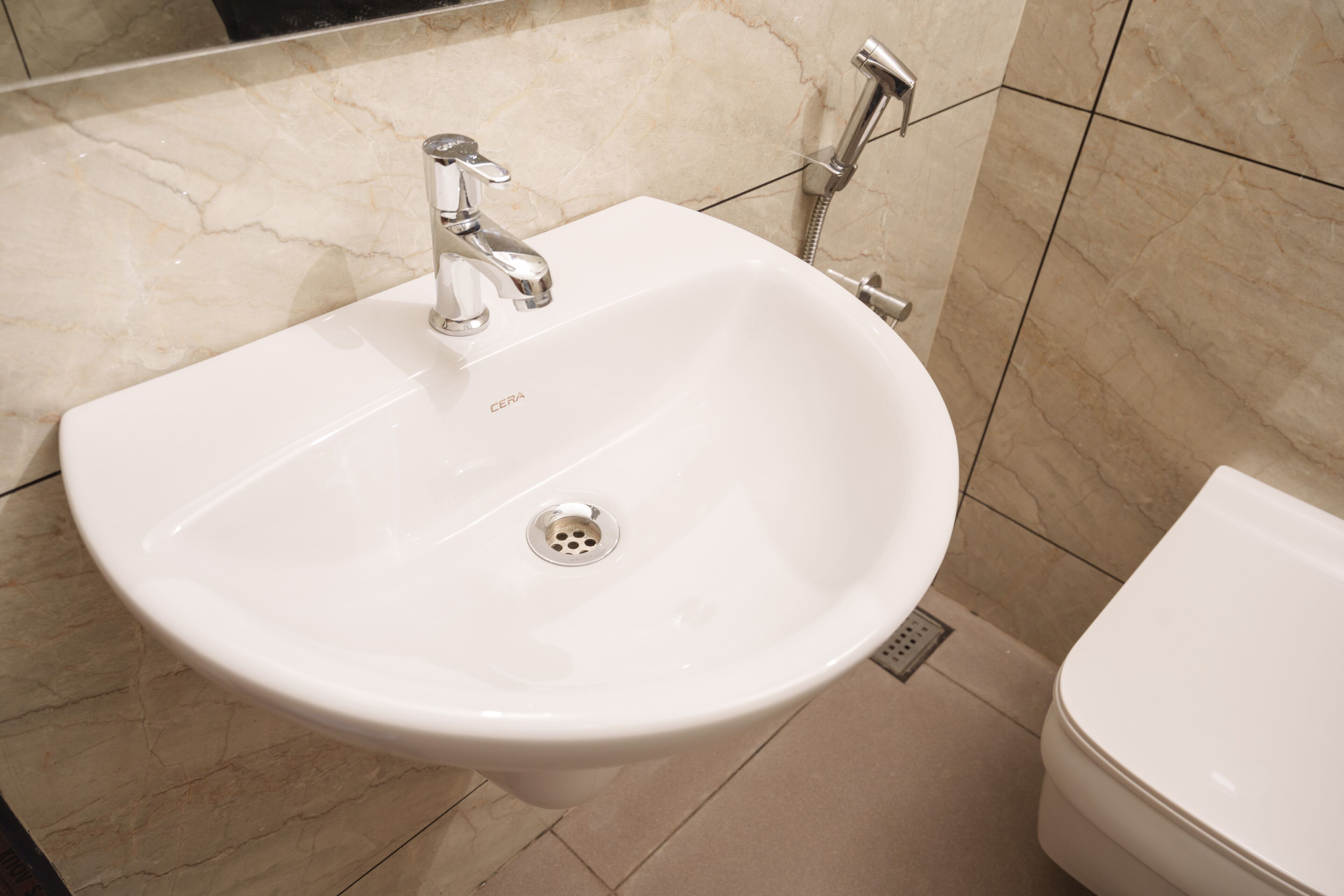 A bathroom with a white pedestal sink, a modern faucet, and a toilet.