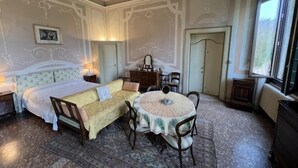 A room with a bed, a sofa, a round table with chairs, a dresser, and a radiator. - Big Scuderia Country mansion_500sqm (San Pietro Viminario)