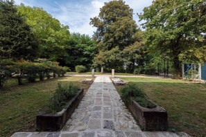 Un sendero de piedra que conduce a un cementerio con lápidas, rodeado de árboles y césped.