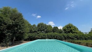 A rectangular swimming pool with clear blue water, surrounded by dense green trees and a clear sky. - Big Scuderia Country mansion_500sqm (San Pietro Viminario)