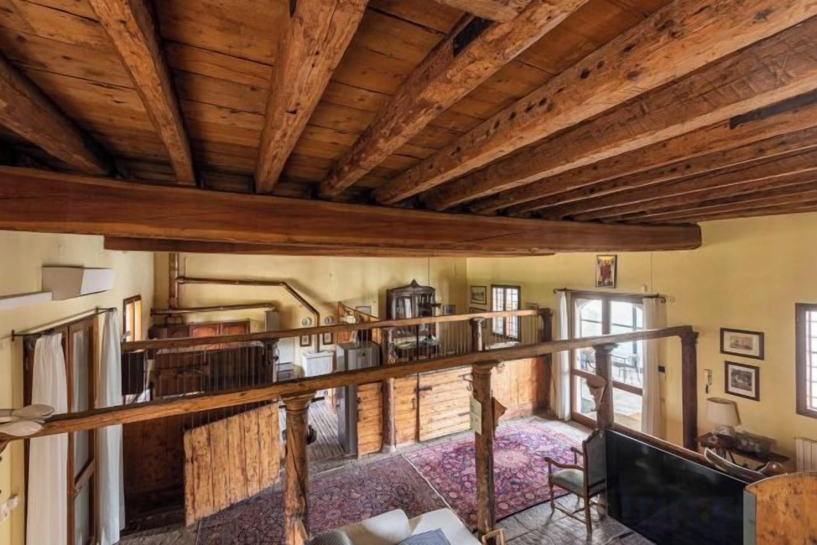 A rustic interior with exposed wooden beams, a staircase, and a view of the outside.