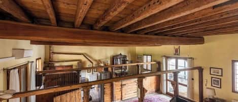 A rustic interior with exposed wooden beams, a staircase, and a view of the outside.