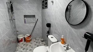 Ein kleines Badezimmer mit Toilette, Waschbecken und Dusche. Auf dem Boden stehen zwei Eimer und ein Wischmopp.