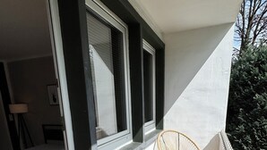 A balcony with a wooden floor, a white railing, and a wicker chair. - Apartment Sana Klinik No 12 Balcony (Offenbach am Main)