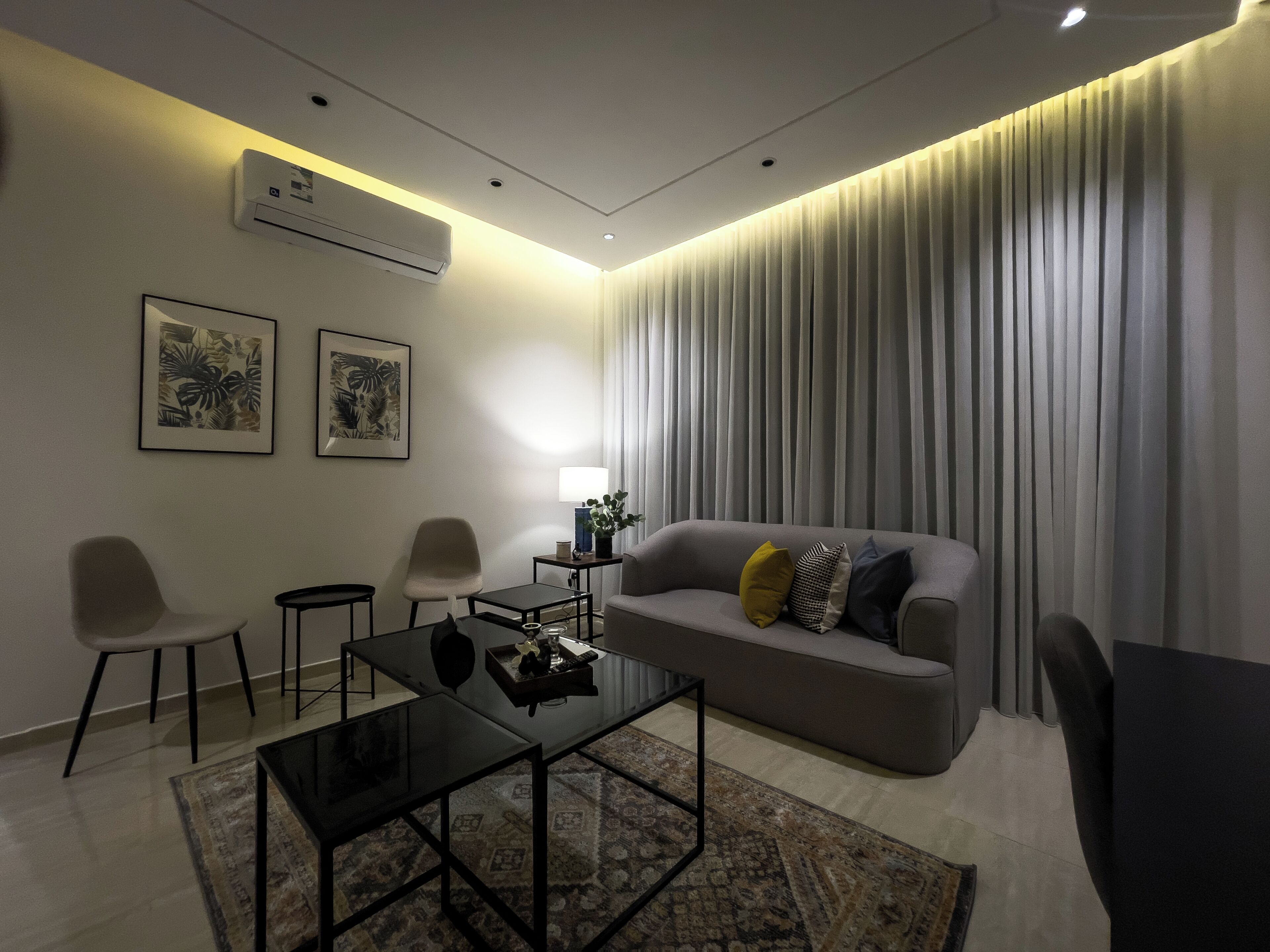 Un salon moderne avec un canapé, deux fauteuils, une table basse et une lampe. Deux tableaux encadrés sont accrochés au mur.