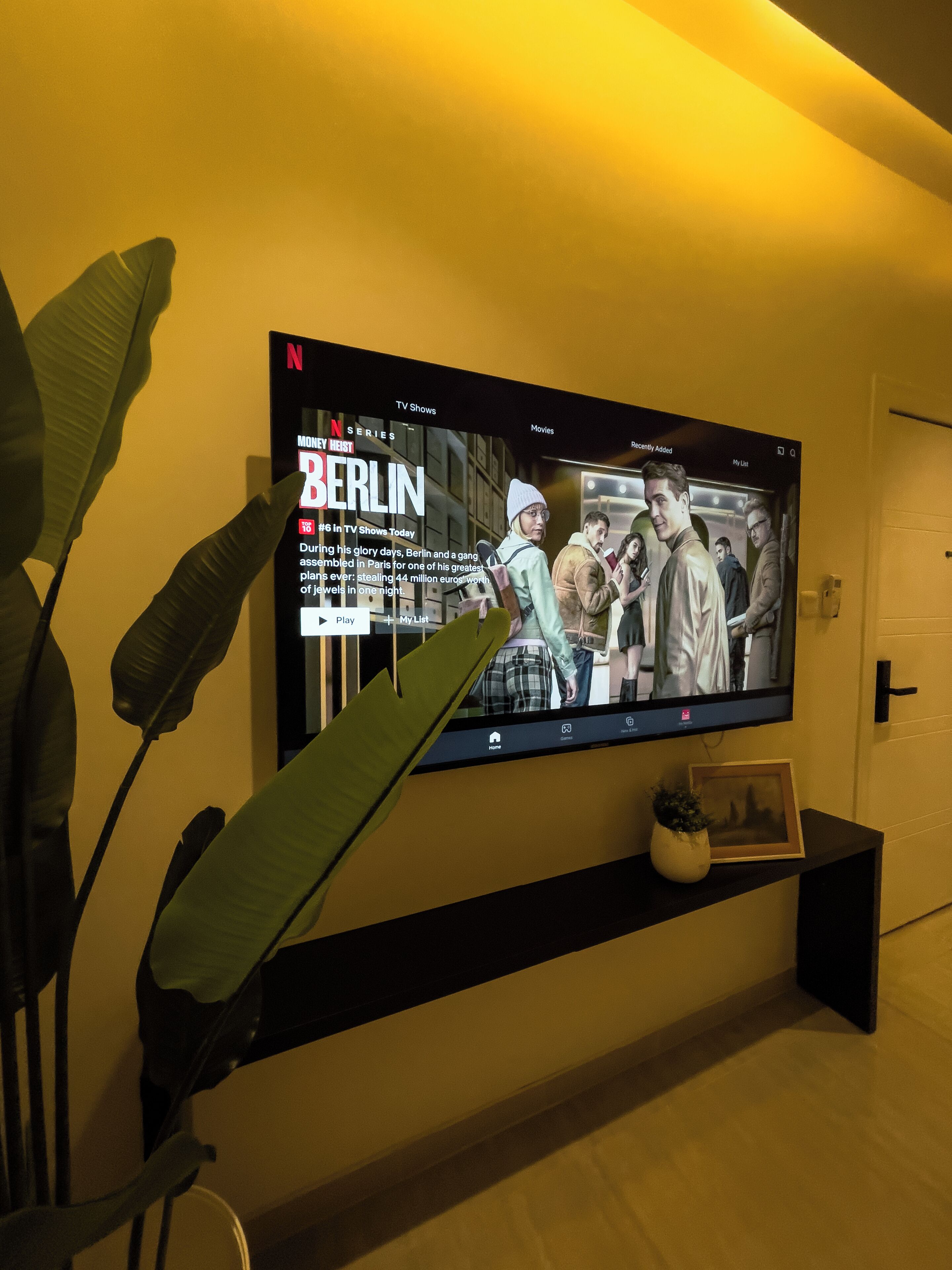 Un téléviseur à écran plat fixé au mur diffuse la série Netflix « La Casa de Papel », et un sous-titre indique qu’il s’agit d’un braquage à Berlin.