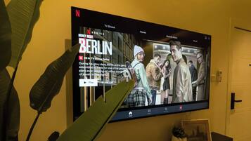 Un téléviseur à écran plat fixé au mur diffuse la série Netflix « La Casa de Papel », et un sous-titre indique qu’il s’agit d’un braquage à Berlin.