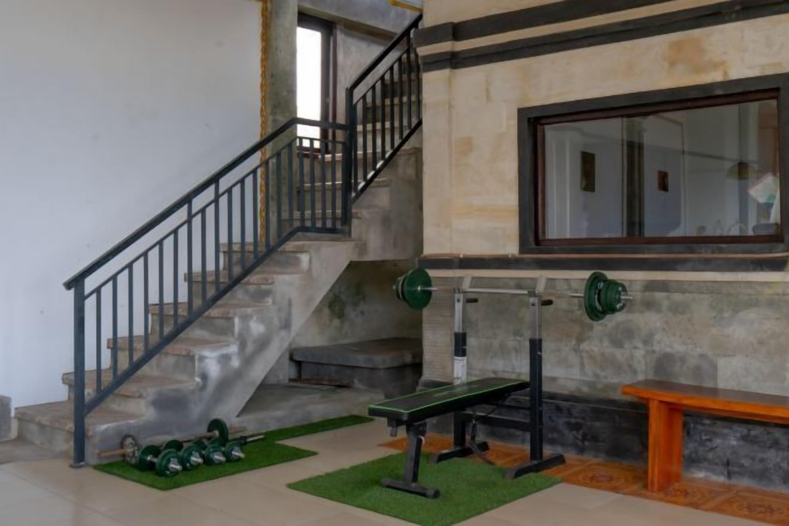 A staircase with a metal railing, a bench, and a weight bench in a room with a stone wall and a window.