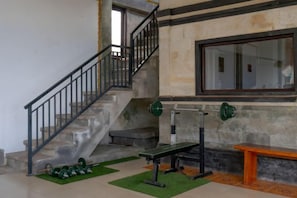 A staircase with a metal railing, a bench, and a weight bench in a room with a stone wall and a window. - Mountain View House Kintamani (Bali)