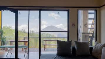 A room with a bed, a balcony with a table and chairs, and a view of a mountain.