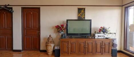 Une pièce avec un téléviseur posé sur un meuble en bois, un vase rempli de fleurs et une grande fenêtre.
