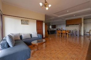 A living room with a sofa, a coffee table, and a kitchen area in the background. - Mountain View House Kintamani (Bali)
