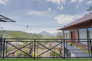A balcony with a view of a mountainous landscape, a brick building with large windows, and a metal railing. - Mountain View House Kintamani (Bali)