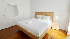 A neatly made bed with white linens and pillows, a wooden headboard, a bedside table with a lamp, and a white wardrobe with a built-in shelf. - 2bedrm unit next to southbank (Highgate Hill)