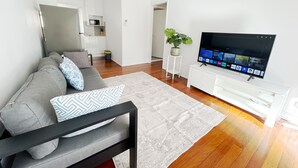 A modern living room with a sofa, TV, and a small kitchen area in the background. - 2bedrm unit next to southbank (Highgate Hill)