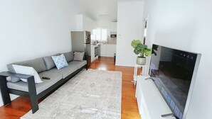 A modern living room with a grey sofa, a flat-screen TV, and a kitchen in the background. - 2bedrm unit next to southbank (Highgate Hill)