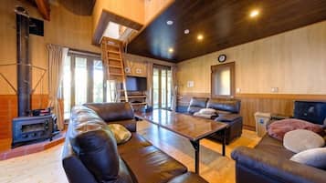 A cozy living room with a fireplace, leather sofas, a wooden table, and a ladder leading to a loft.