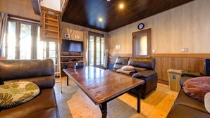 Un salon chaleureux avec une table en bois, des canapés en cuir, un téléviseur et un escalier menant à une mezzanine.
