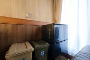A room with a wooden wall, a black refrigerator, a beige trash bin, and a grey sofa. - SOMEDAY (Onjuku)