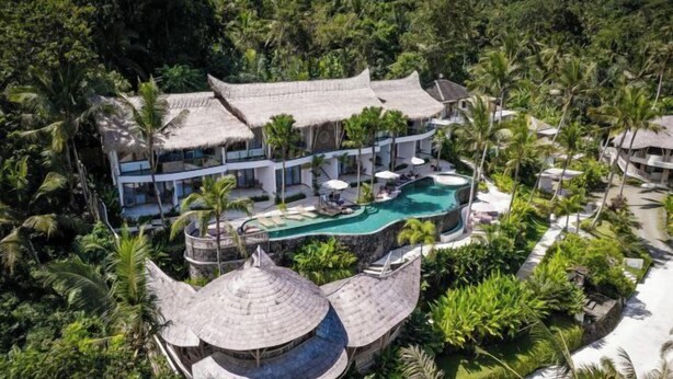 Un resort con piscina, construcciones de techo de paja y exuberante vegetación.