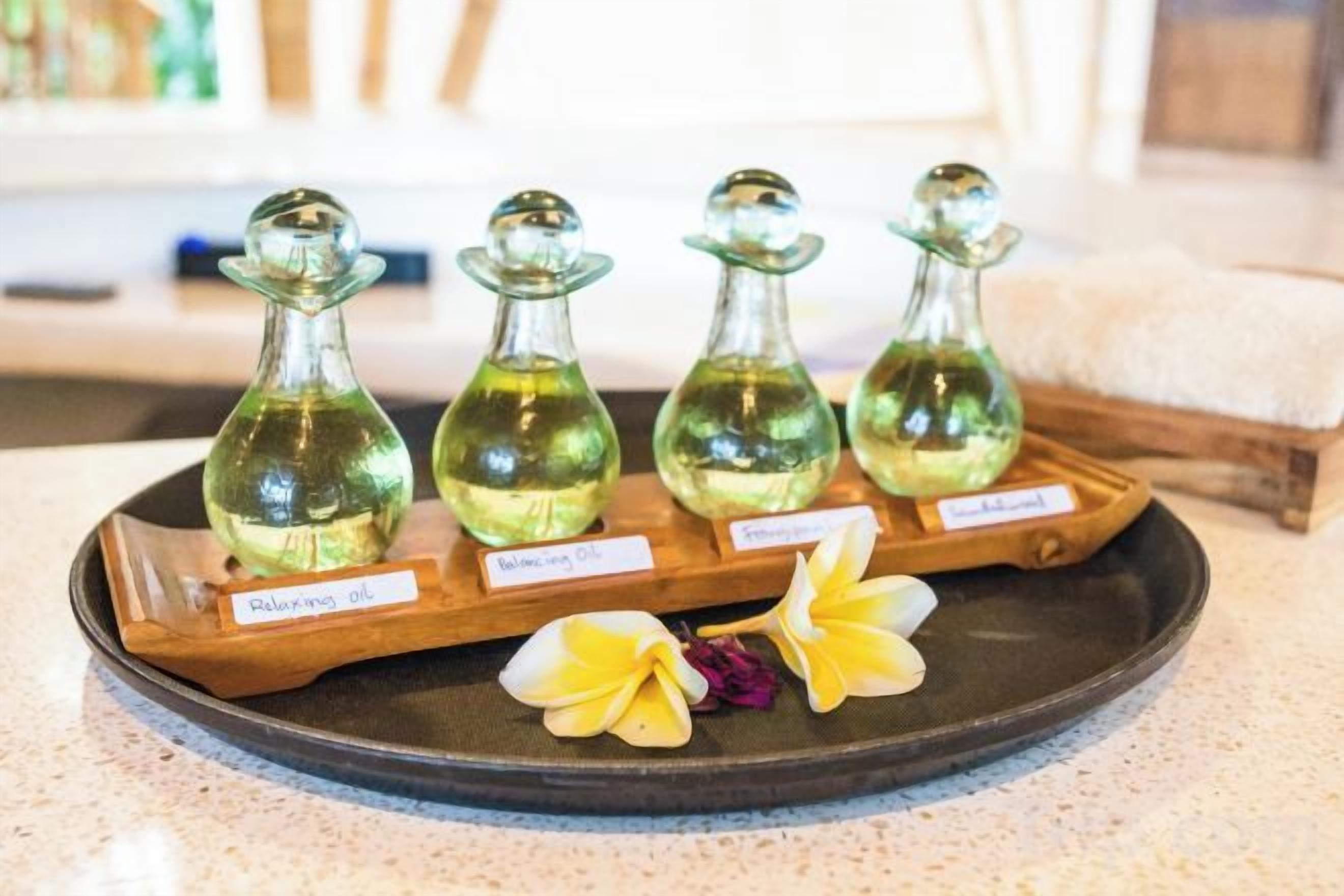 Cuatro botellas de vidrio con etiquetas sobre una bandeja, probablemente conteniendo aceites esenciales, con una flor al frente.